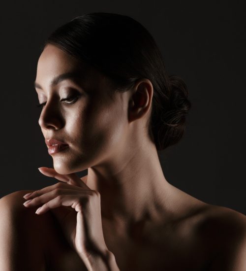 portrait-of-sensual-beautiful-woman-looking-aside-while-touching-her-chin-in-low-lights-isolated-over-black